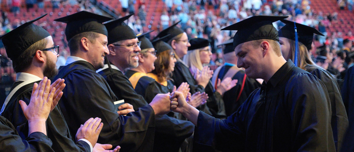 SCC graduate fist pumps with instructors at the May 2023 graduation. 