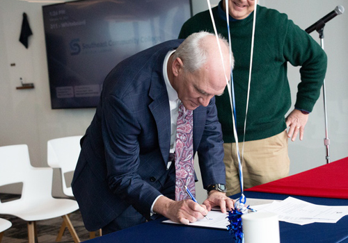 Dr. Paul Illich signs articulation agreement in a blue suit and paisley necktie. 