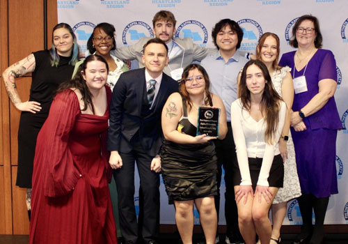 A group of ten people pose together. One person in the center holds a glass award plaque for the Alpha Pi Lambda chapter.