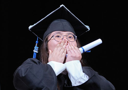 A female graduate in cap and gown covers their mouth with both hands after receiving their degree at the 2025 Southeast Community College Spring Graduation ceremony.
