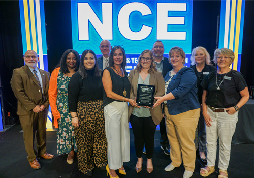 Representatives from Southeast Community College, Central Community College, and Northeast Community College stand in front of a large blue screen displaying 