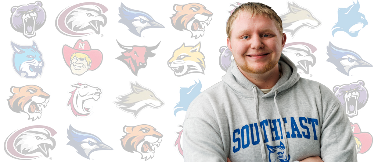 Male student with blonde hair, wearing a Bobcat hoodie is standing in front of Nebraska college mascots. 