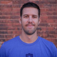 Chad Wilken is in a blue shirt standing in front of a brick wall. 
