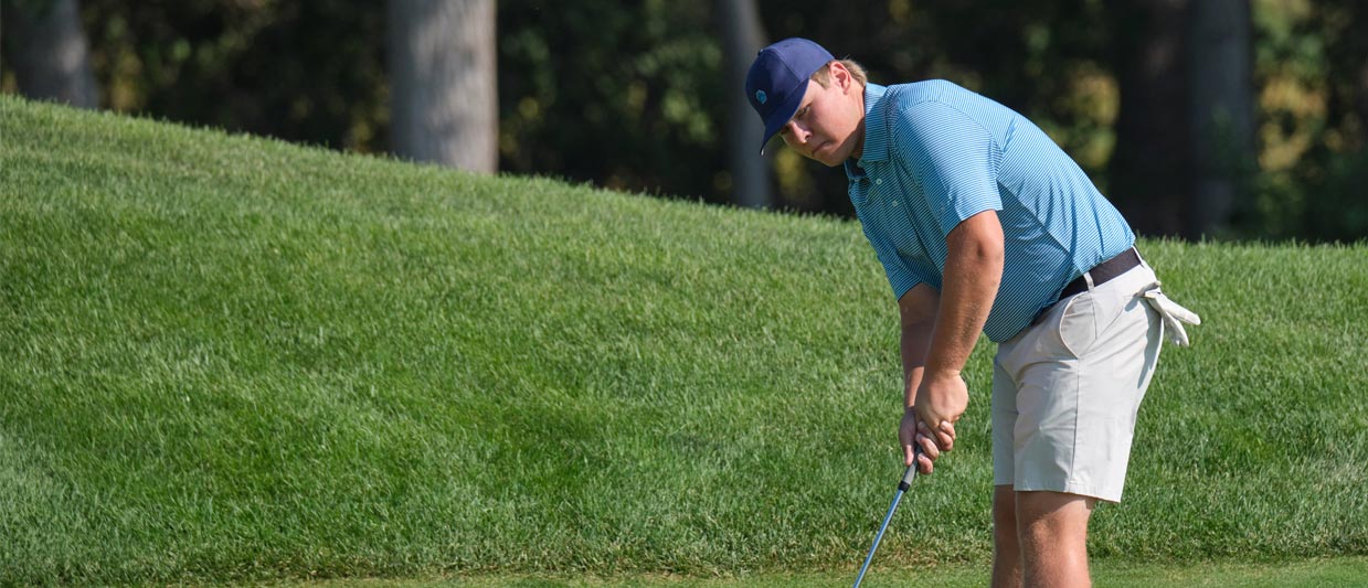Hayden Delaloye hits a put in a golf tournament, wearing a blue hat and light blue shirt