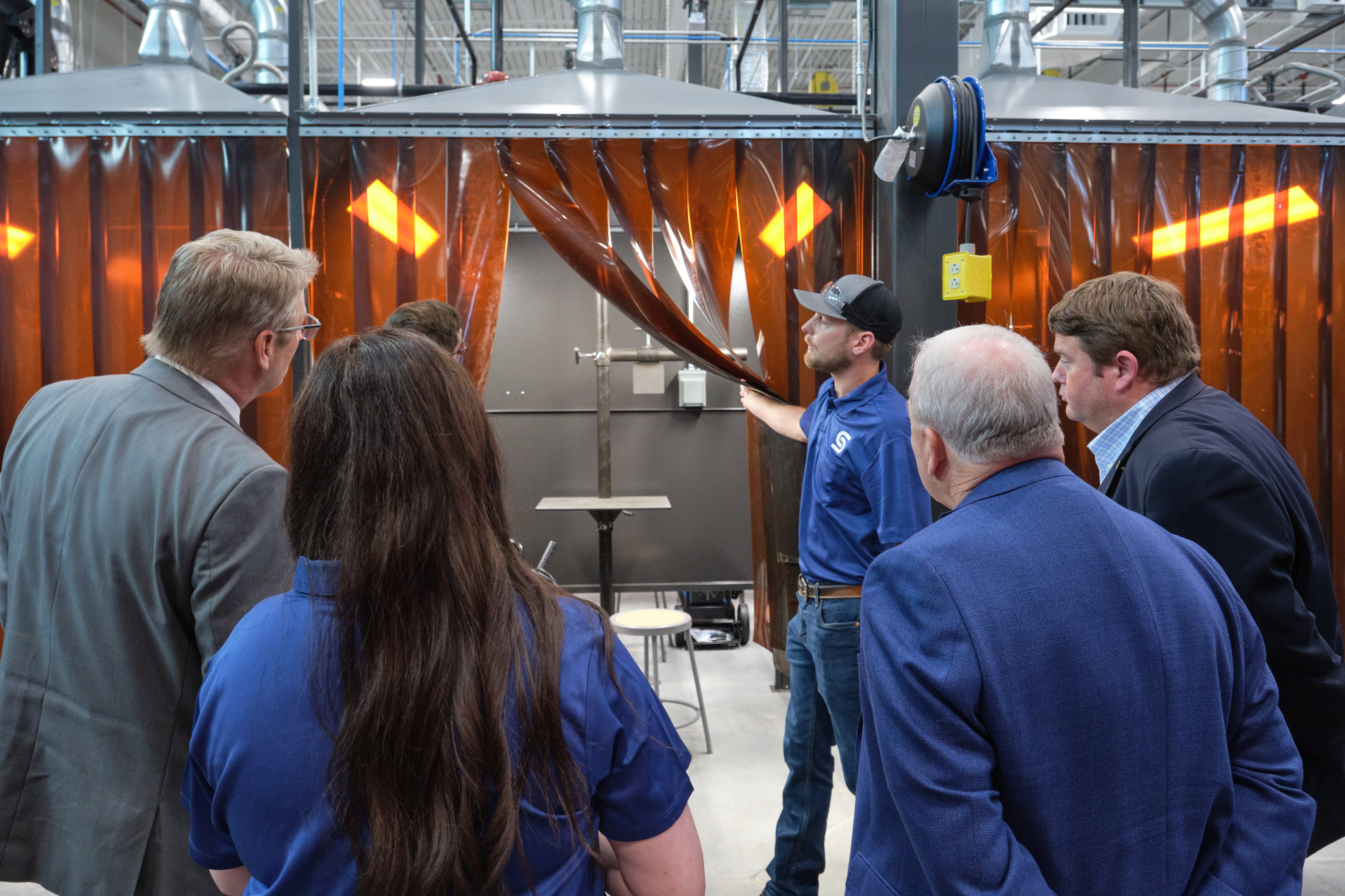 Guests get a first look inside one of the advanced welding booths as the curtain is pulled back during the grand opening celebration