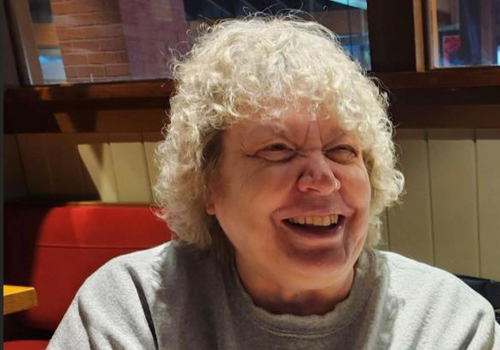 Becky Bauer is smiling at a restaurant in a gray sweatshirt. 